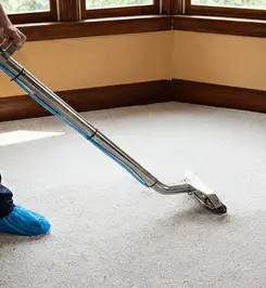Steam carpet cleaning technician using a hot-water extraction wand on a residential carpet, wearing blue protective shoe covers Columbus, OH.