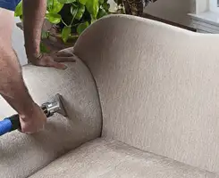 Professional upholstery cleaner deep-cleaning a fabric sofa with a handheld extraction tool and hose in Columbus, OH.